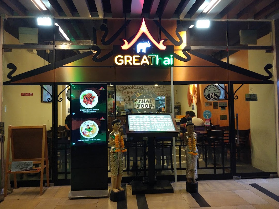 The illuminated storefront of GreaThai, a Thai restaurant, featuring digital displays and traditional decor.