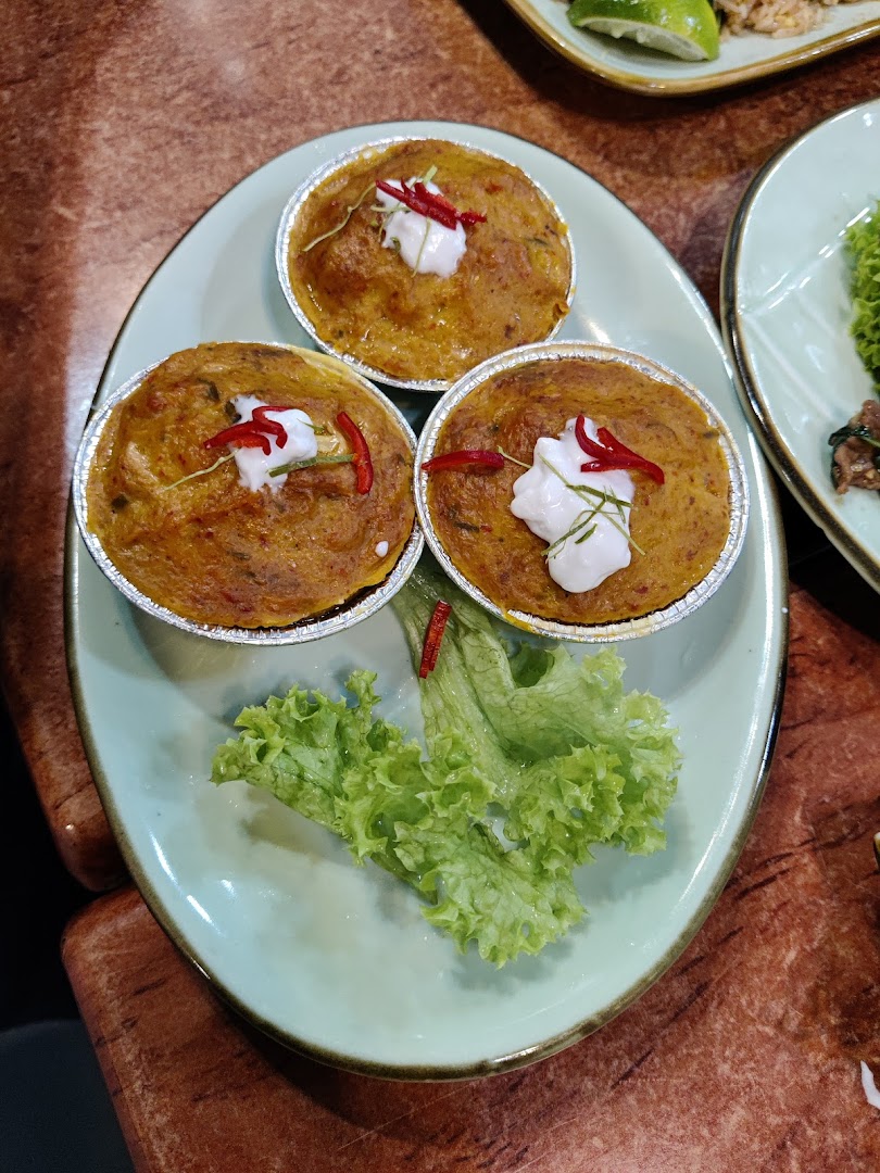 Three individual servings of a savory Thai dish, garnished with cream, chili, and kaffir lime leaves.