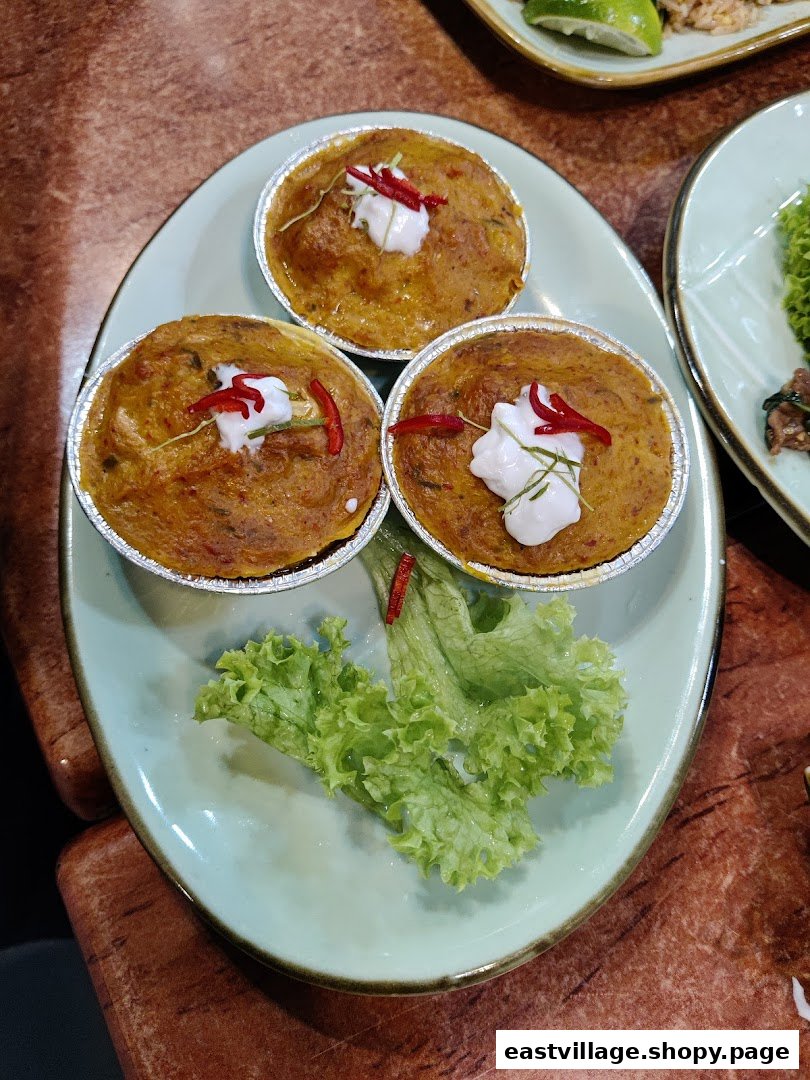 Three individual servings of a savory Thai dish, garnished with cream, chili, and kaffir lime leaves.