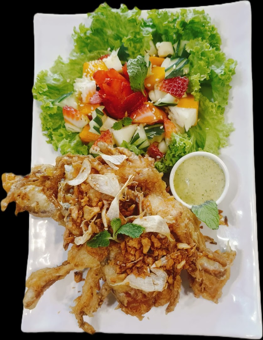 A plate of crispy fried soft-shell crab with garlic, served alongside a vibrant fruit salad and dipping sauce.