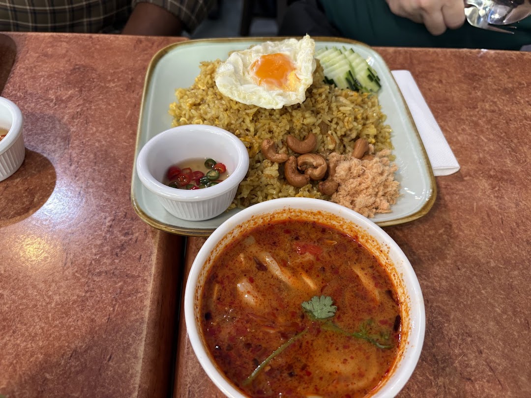 A vibrant Thai meal featuring fried rice with a fried egg, cashews, and a side of spicy Tom Yum soup.