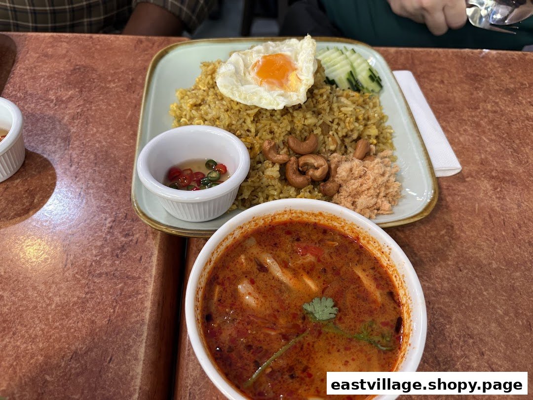 A vibrant Thai meal featuring fried rice with a fried egg, cashews, and a side of spicy Tom Yum soup.