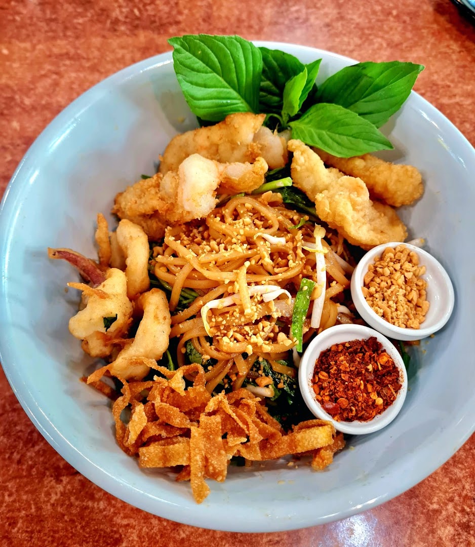 A vibrant bowl of Thai noodles with crispy fried seafood, fresh basil, and condiments.