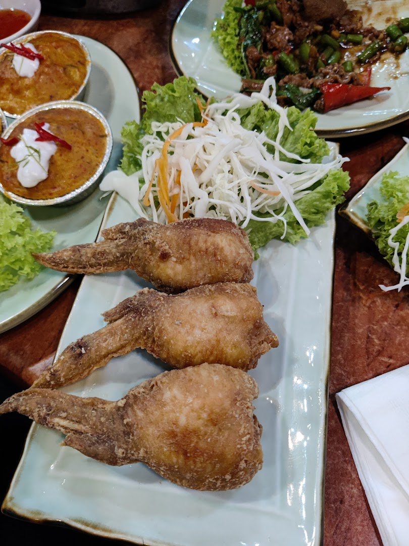 A close-up of delicious Thai dishes, including crispy fried chicken wings and steamed curries, served on a table.