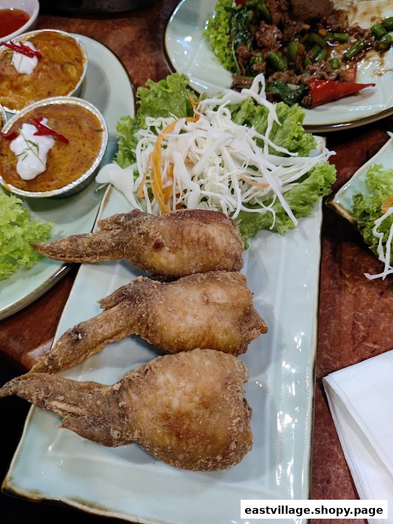 A close-up of delicious Thai dishes, including crispy fried chicken wings and steamed curries, served on a table.