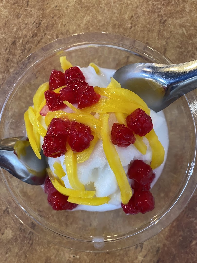 A vibrant Thai dessert featuring white ice cream, yellow jackfruit strips, and red water chestnuts in a clear cup.