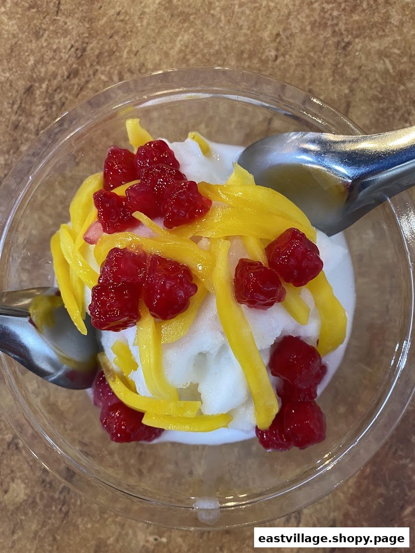 A vibrant Thai dessert featuring white ice cream, yellow jackfruit strips, and red water chestnuts in a clear cup.