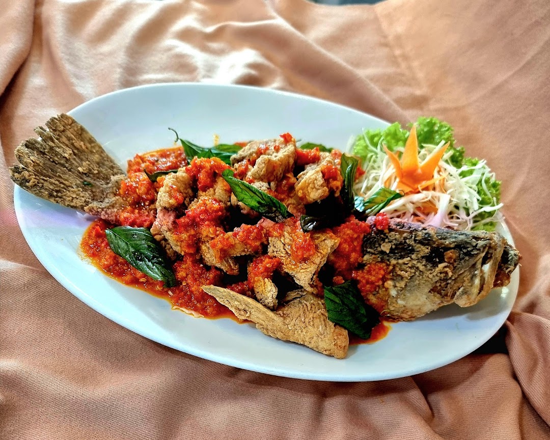 A whole fried fish dish generously topped with a vibrant red chili sauce and fresh basil leaves.