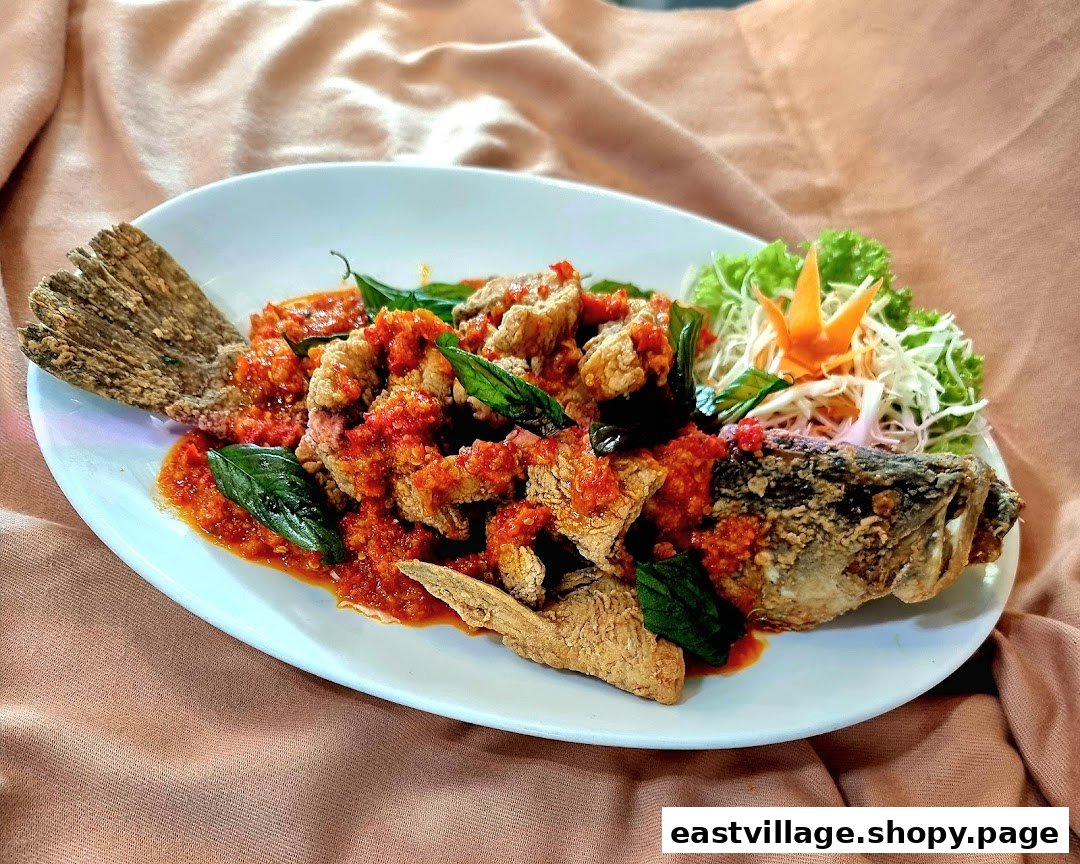 A whole fried fish dish generously topped with a vibrant red chili sauce and fresh basil leaves.
