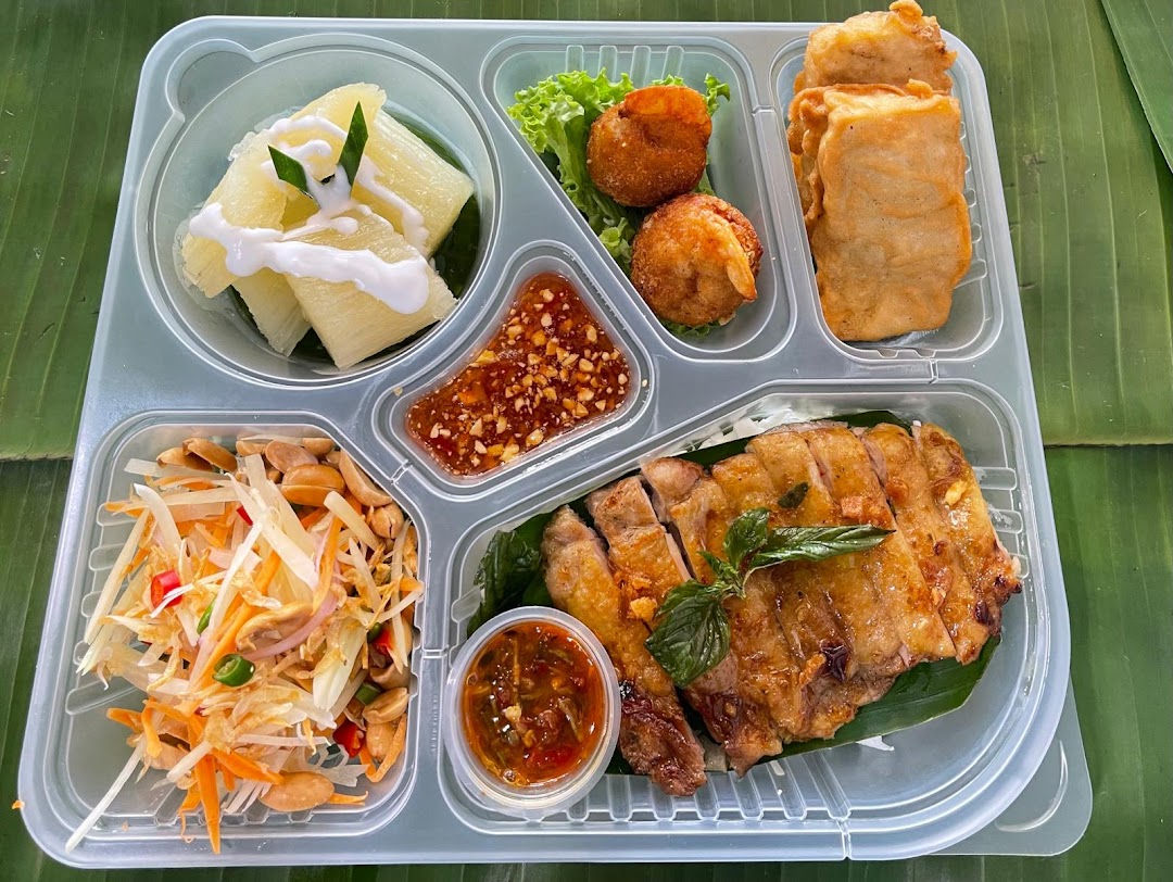 A vibrant GreaThai bento box featuring grilled chicken, papaya salad, and dessert.