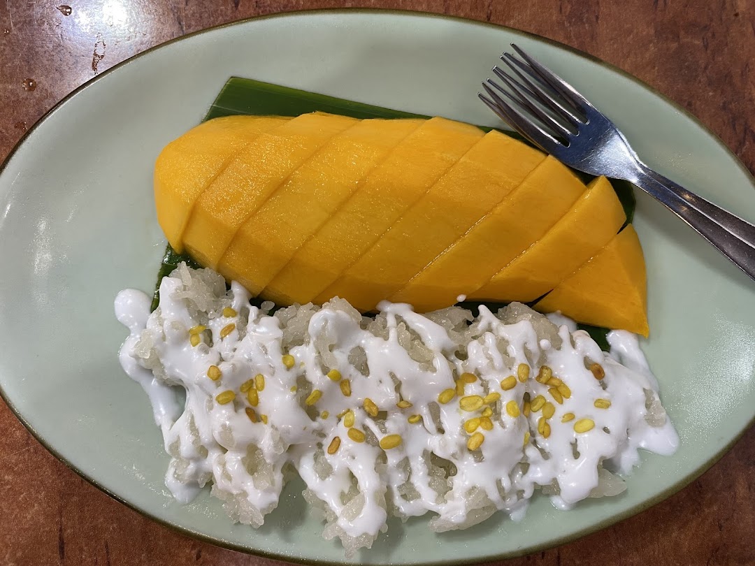 A vibrant plate of mango sticky rice with coconut milk and a fork on a light green plate.