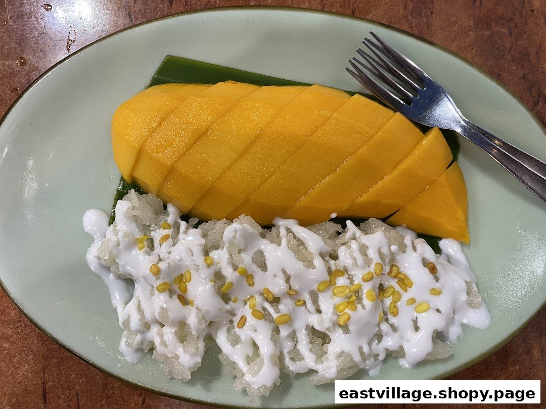 A vibrant plate of mango sticky rice with coconut milk and a fork on a light green plate.