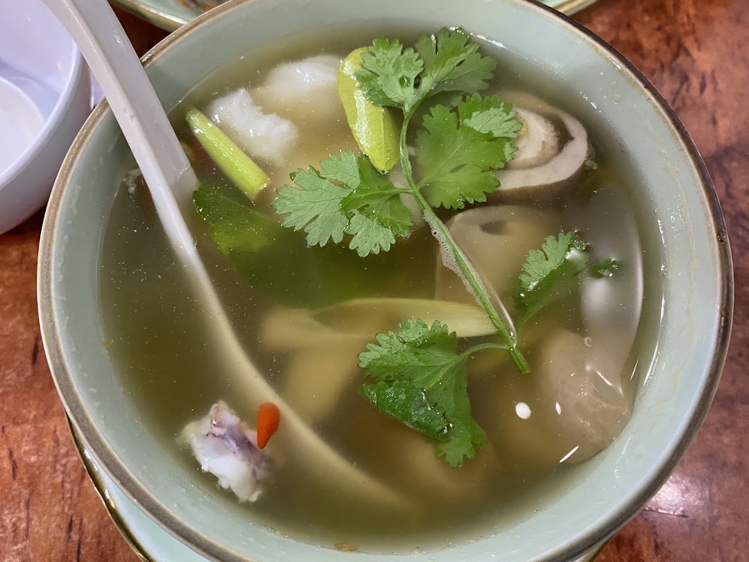 A close-up of a clear Thai soup with herbs, mushrooms, and meat in a light green bowl.