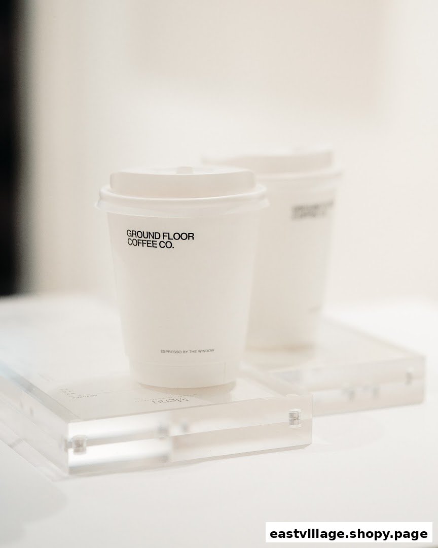 Two minimalist white coffee cups from Ground Floor Coffee Co. displayed on a clear stand.