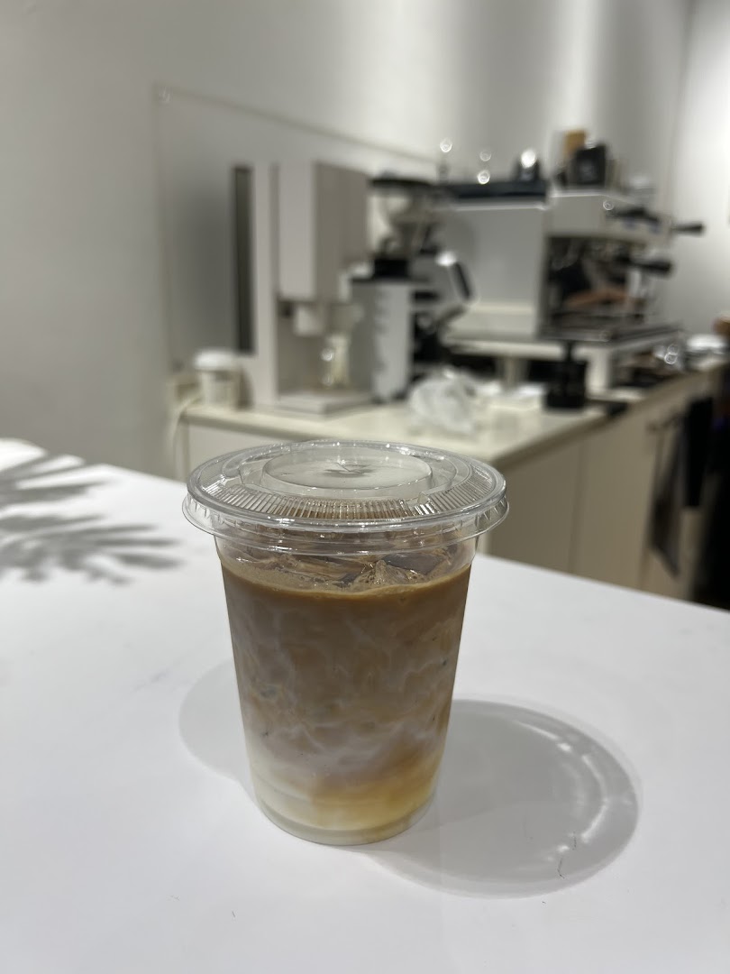 An iced coffee drink with layered milk and coffee on a white counter, with coffee equipment in the background.