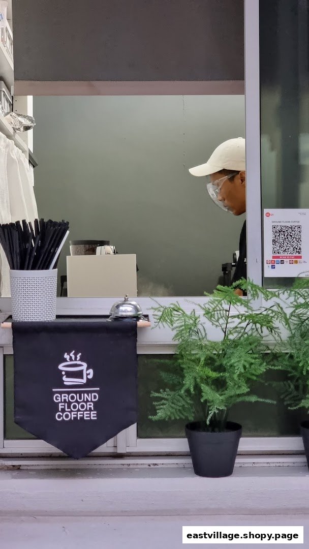 A staff member at Ground Floor Coffee's service window, featuring branding, payment QR, and convenient service.