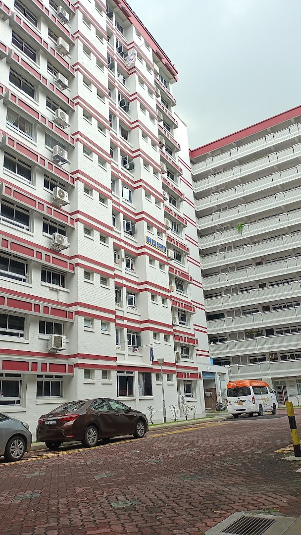 A street view of residential buildings with red and white facades, parked cars, and a paved road.