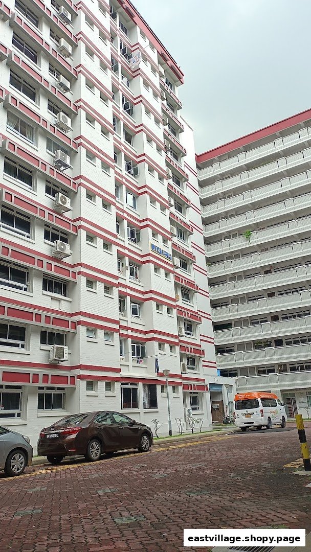 A street view of residential buildings with red and white facades, parked cars, and a paved road.