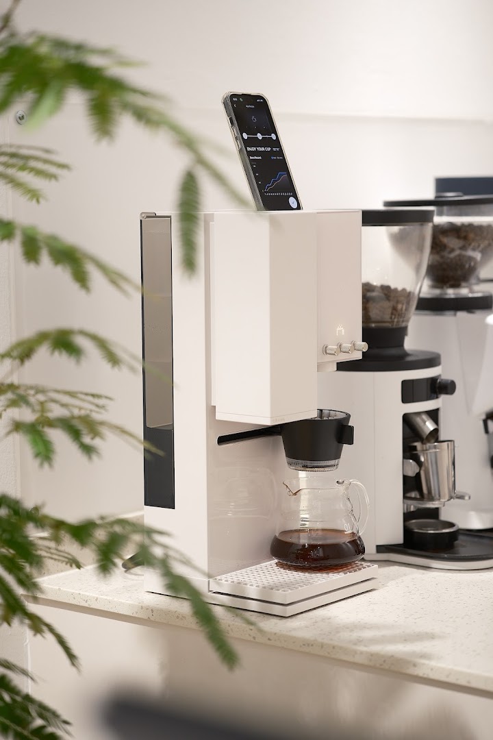 A modern coffee machine brewing coffee, with a smartphone displaying brewing metrics.