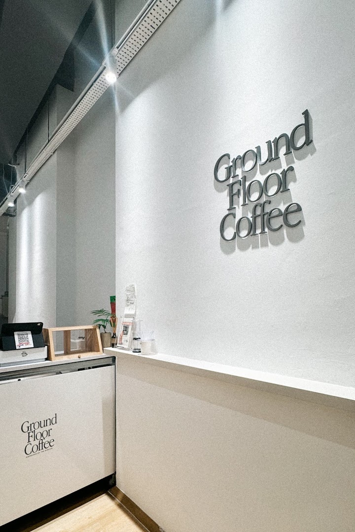 A clean, modern interior view of Ground Floor Coffee, featuring its prominent wall signage and counter area.
