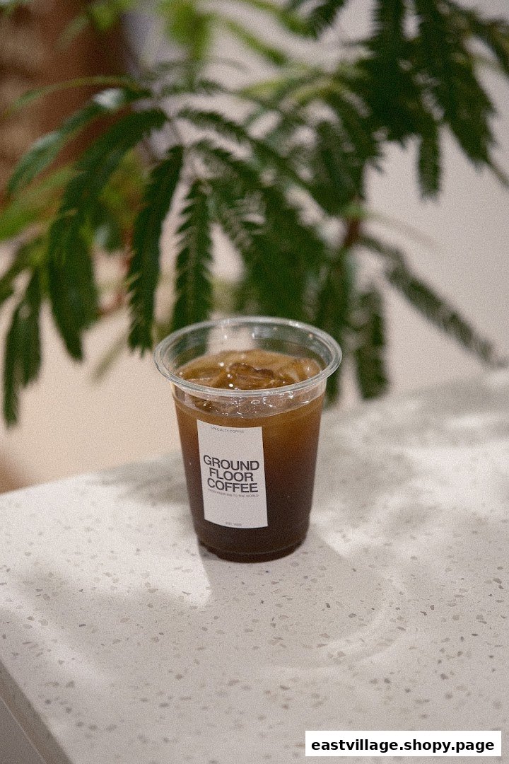 A refreshing iced coffee in a branded cup from Ground Floor Coffee, set on a light counter with green foliage.