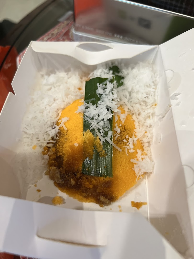 A close-up of a delicious Putu Piring dessert in a white takeaway box, topped with grated coconut.