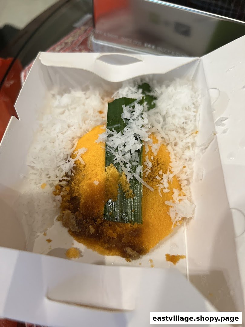 A close-up of a delicious Putu Piring dessert in a white takeaway box, topped with grated coconut.