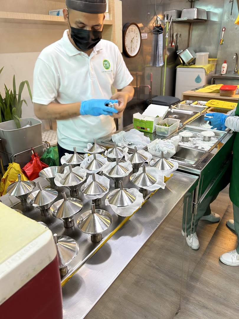 Staff preparing putu piring using traditional molds in a bustling kitchen.