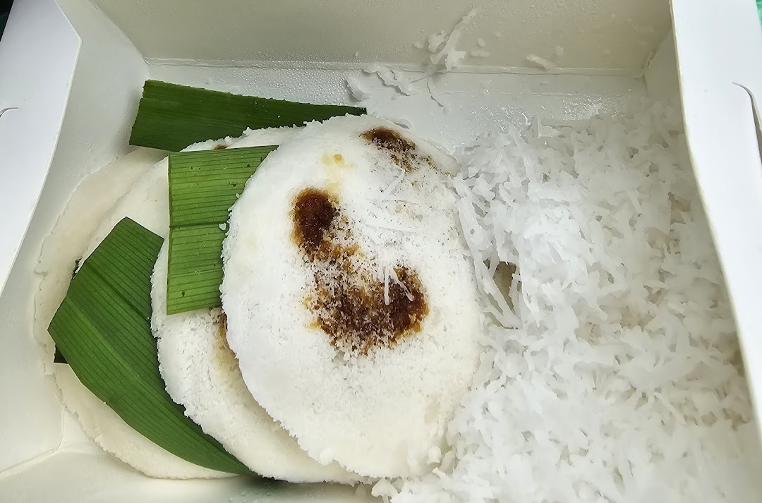 Close-up of traditional putu piring with grated coconut and pandan leaves in a takeaway box.