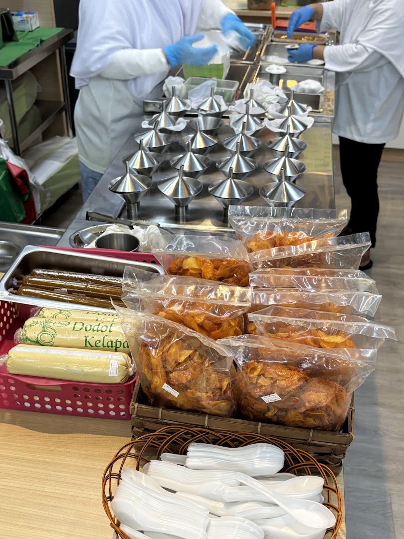 Staff preparing putu piring with traditional molds, alongside packaged snacks and sweets.