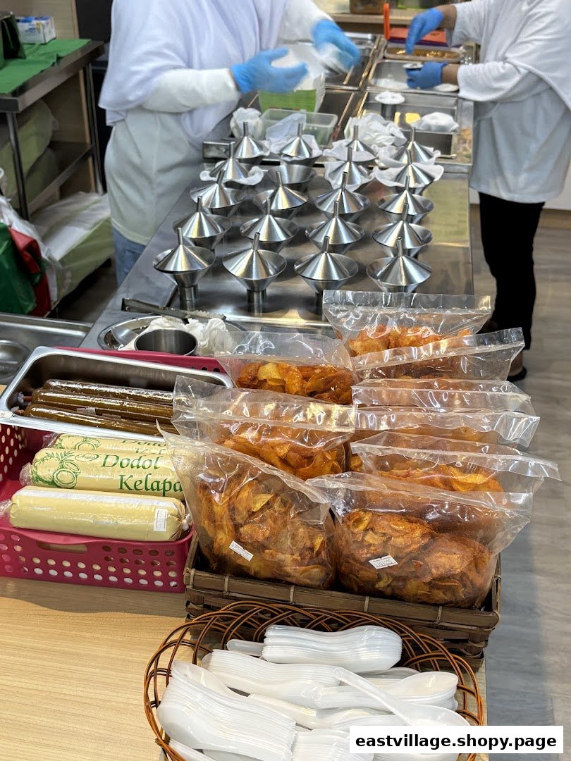 Staff preparing putu piring with traditional molds, alongside packaged snacks and sweets.
