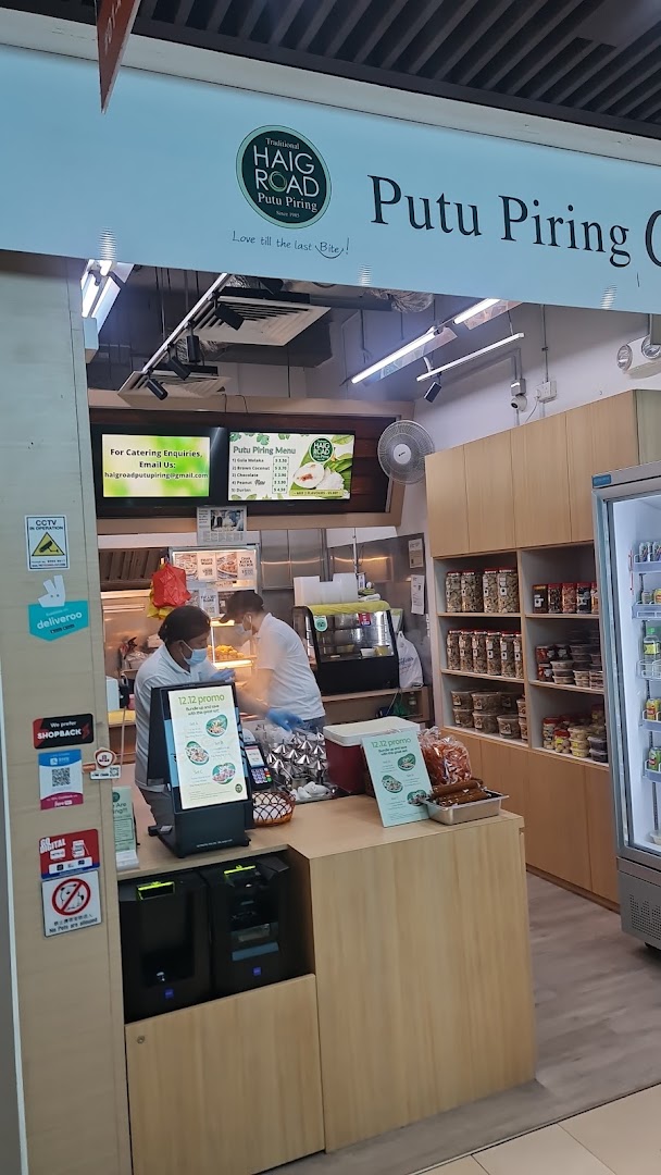 Interior view of Haig Road Putu Piring, showing staff, traditional snacks, and a menu display.