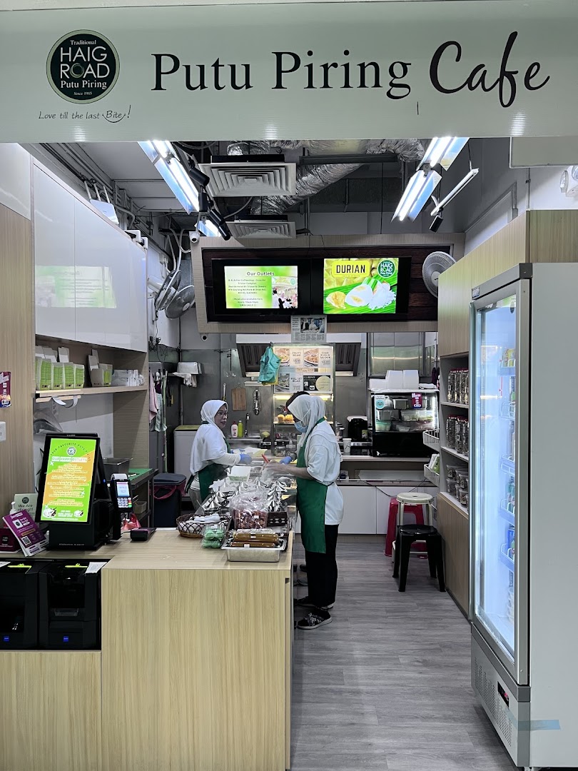 Two staff members serve customers at the counter of Haig Road Putu Piring Cafe.