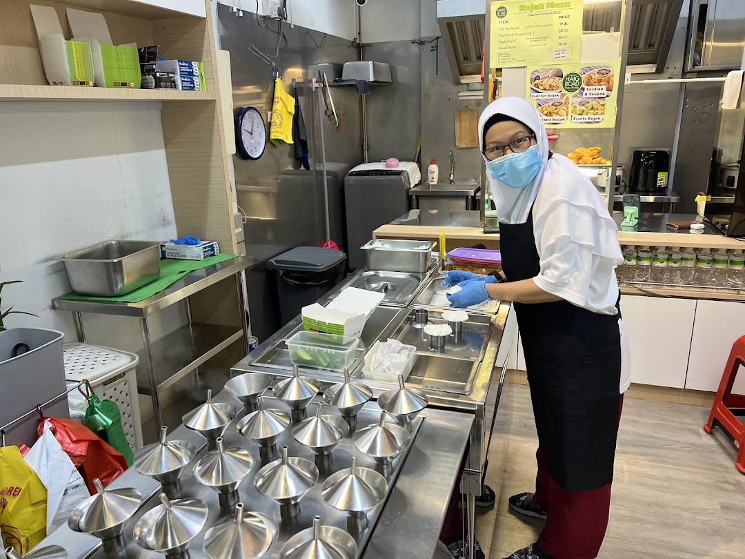 A staff member prepares traditional putu piring in a clean, bustling kitchen.