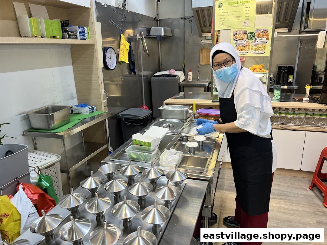 A staff member prepares traditional putu piring in a clean, bustling kitchen.