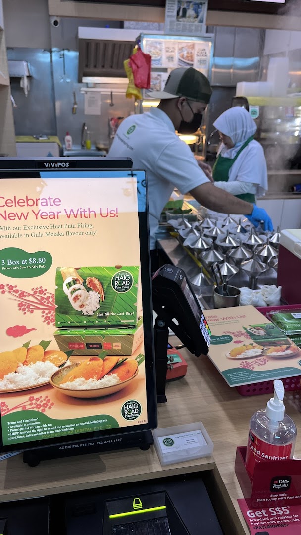 A promotional display for Haig Road Putu Piring's New Year offer, with staff preparing food.