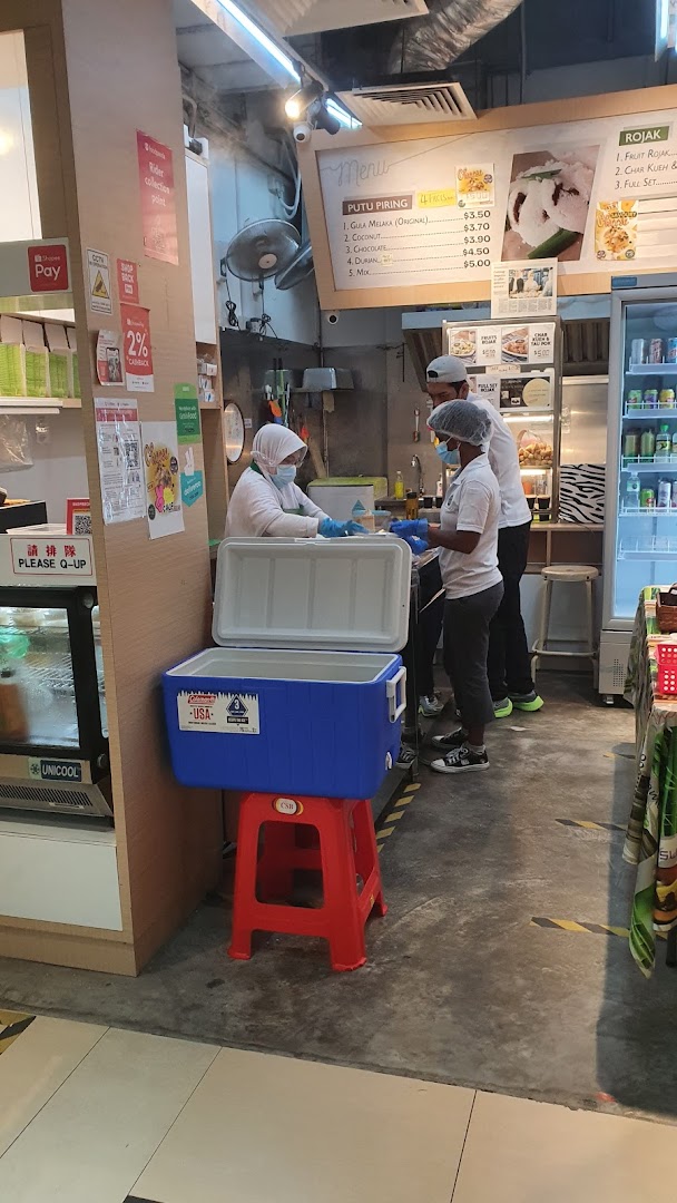 Staff prepare traditional Putu Piring and Rojak behind a counter in a bustling shop interior.