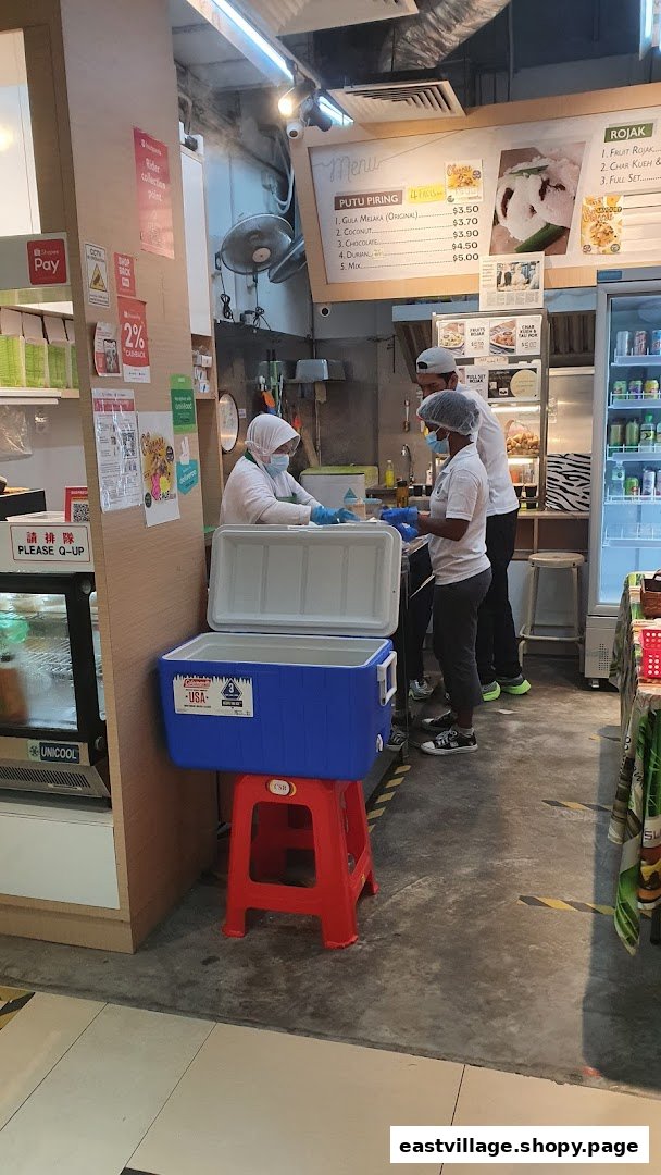 Staff prepare traditional Putu Piring and Rojak behind a counter in a bustling shop interior.