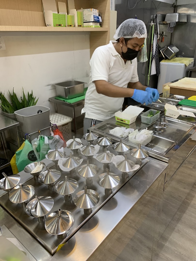 A chef meticulously prepares putu piring, filling traditional metal molds in a clean kitchen.