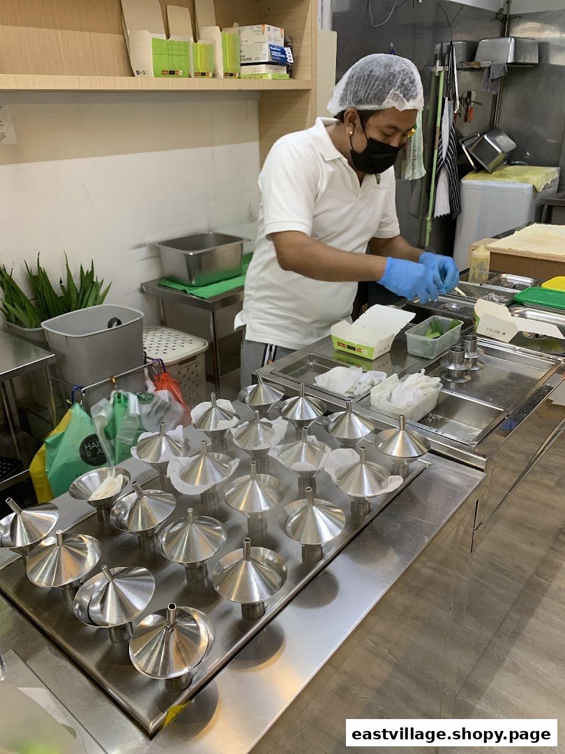A chef meticulously prepares putu piring, filling traditional metal molds in a clean kitchen.