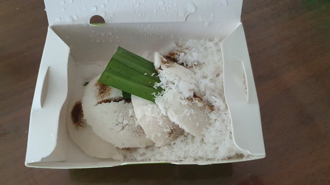 Steamed putu piring with grated coconut and palm sugar in a white takeaway box.