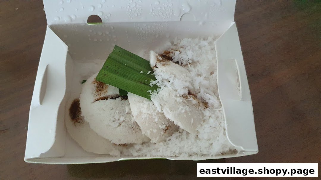 Steamed putu piring with grated coconut and palm sugar in a white takeaway box.