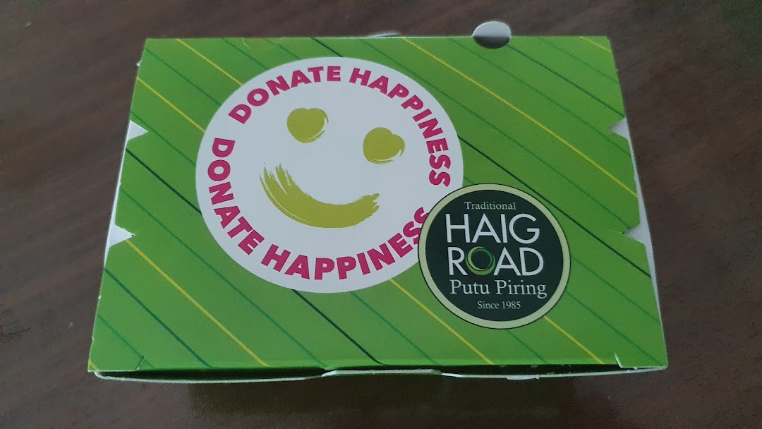 A green product box from Haig Road Putu Piring featuring a 'Donate Happiness' smiley logo.