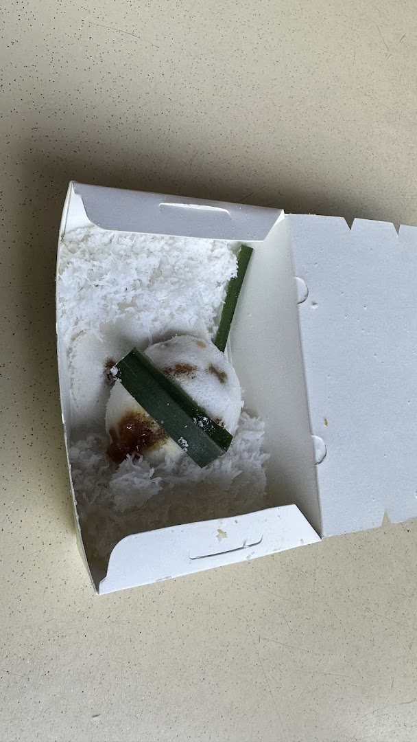 A single putu piring dessert in a white box, garnished with pandan leaves and shredded coconut.