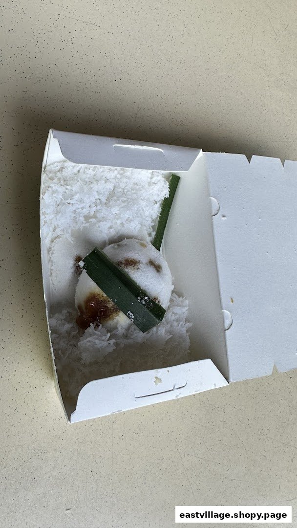 A single putu piring dessert in a white box, garnished with pandan leaves and shredded coconut.