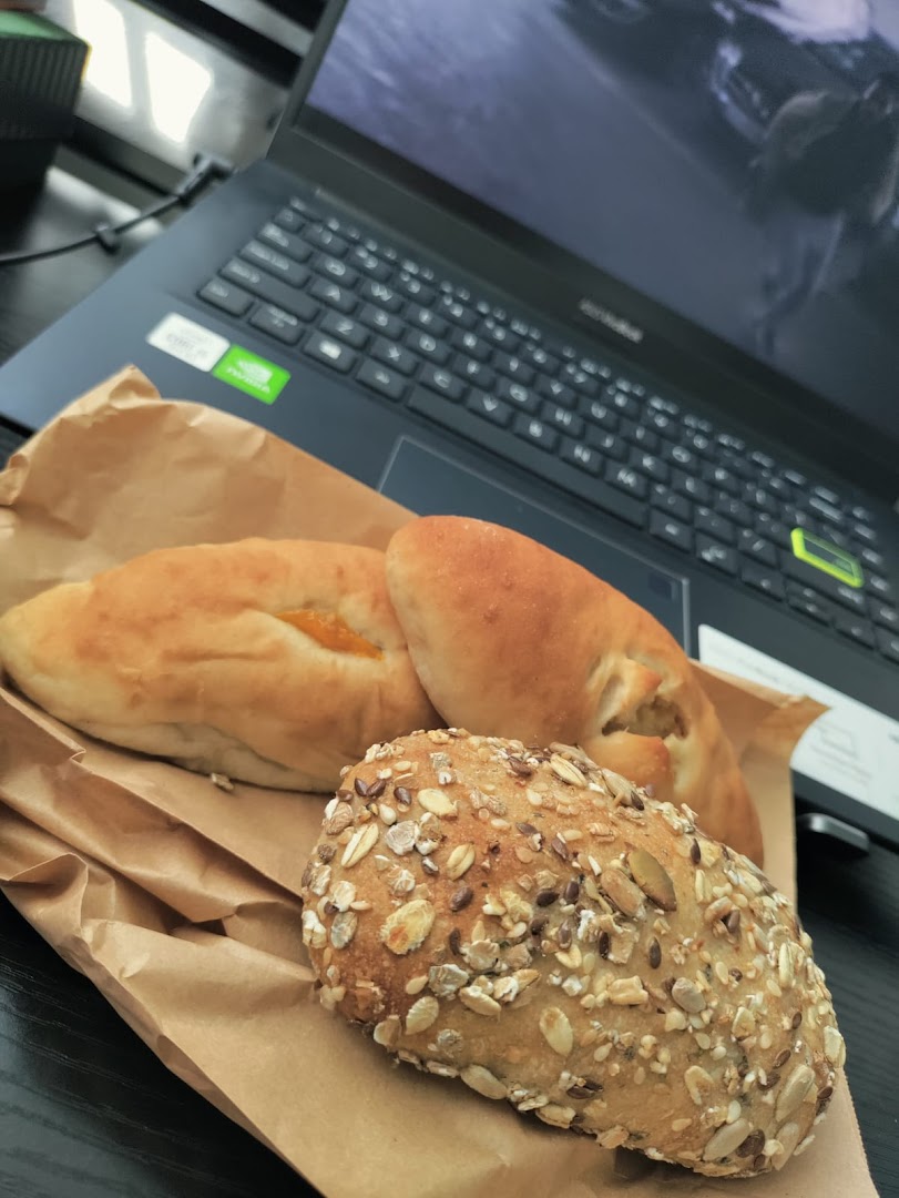 Assorted baked goods, including a multi-grain bun and filled pastries, on a paper bag next to a laptop.