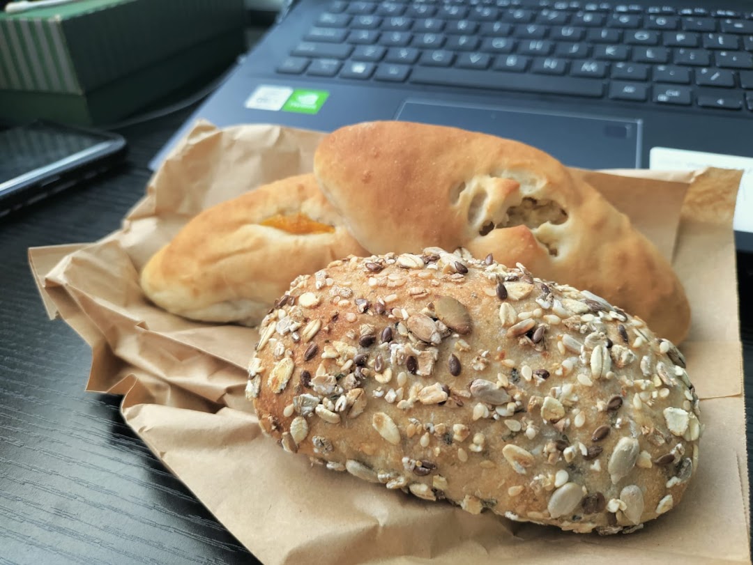 An assortment of freshly baked buns, including a seeded bun and fruit-filled pastries, on brown paper.
