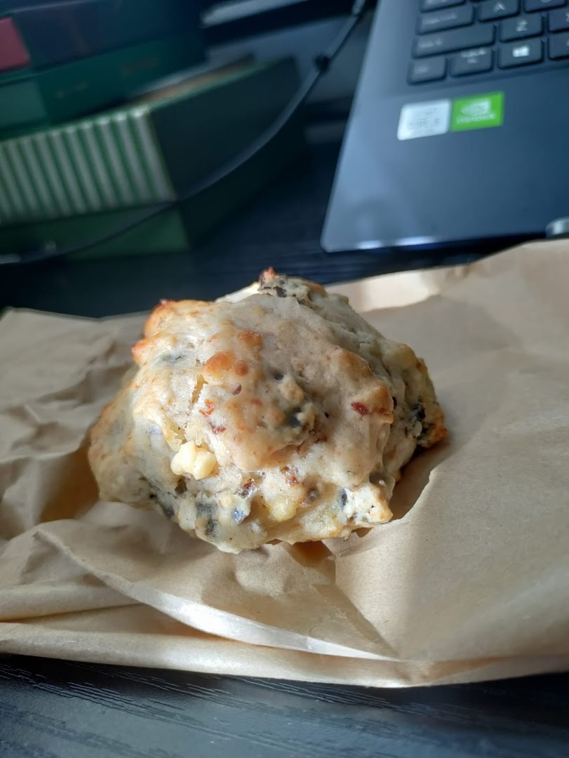A freshly baked, savory bun or scone from HappiBuns, wrapped in brown paper.