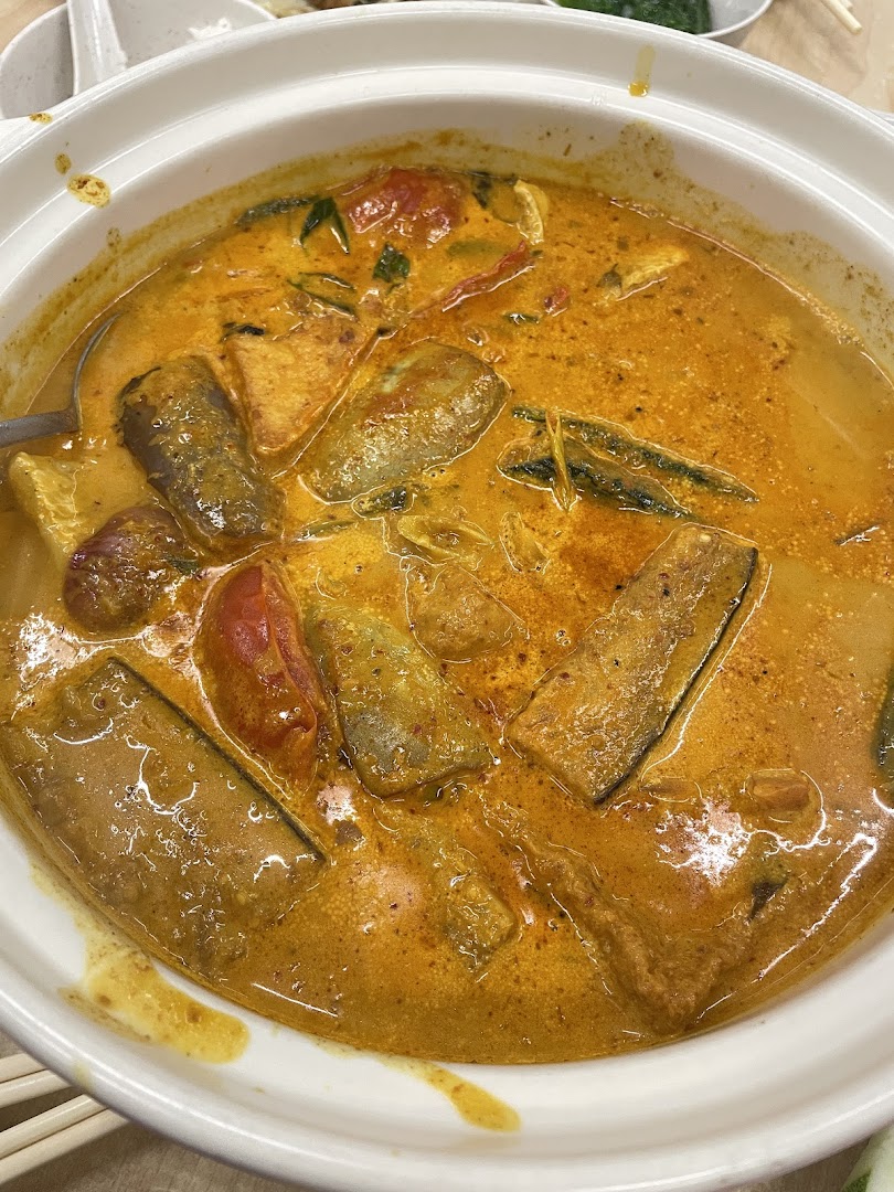 A vibrant pot of rich, spicy curry with fish, vegetables, and tofu in a white ceramic pot.