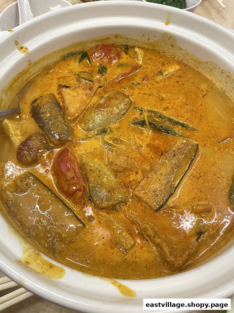 A vibrant pot of rich, spicy curry with fish, vegetables, and tofu in a white ceramic pot.